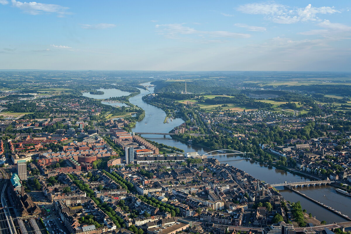 Luchtfoto Maastricht met de Maas die door de stad loopt. Aan beide kanten van de stad zie huizen. Drie bruggen lopen over de Maas.