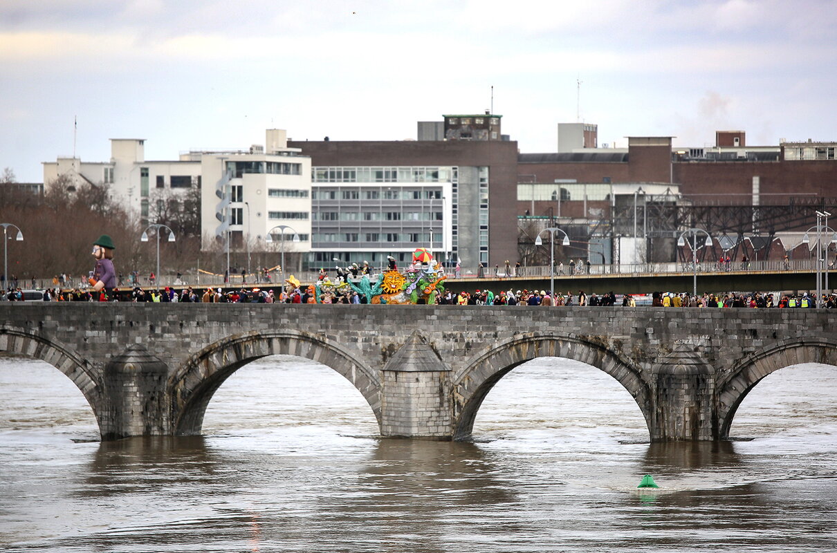 Carnavalsoptocht over de St. Servaasbrug in Maastricht op de achtergrond zie gebouwen.