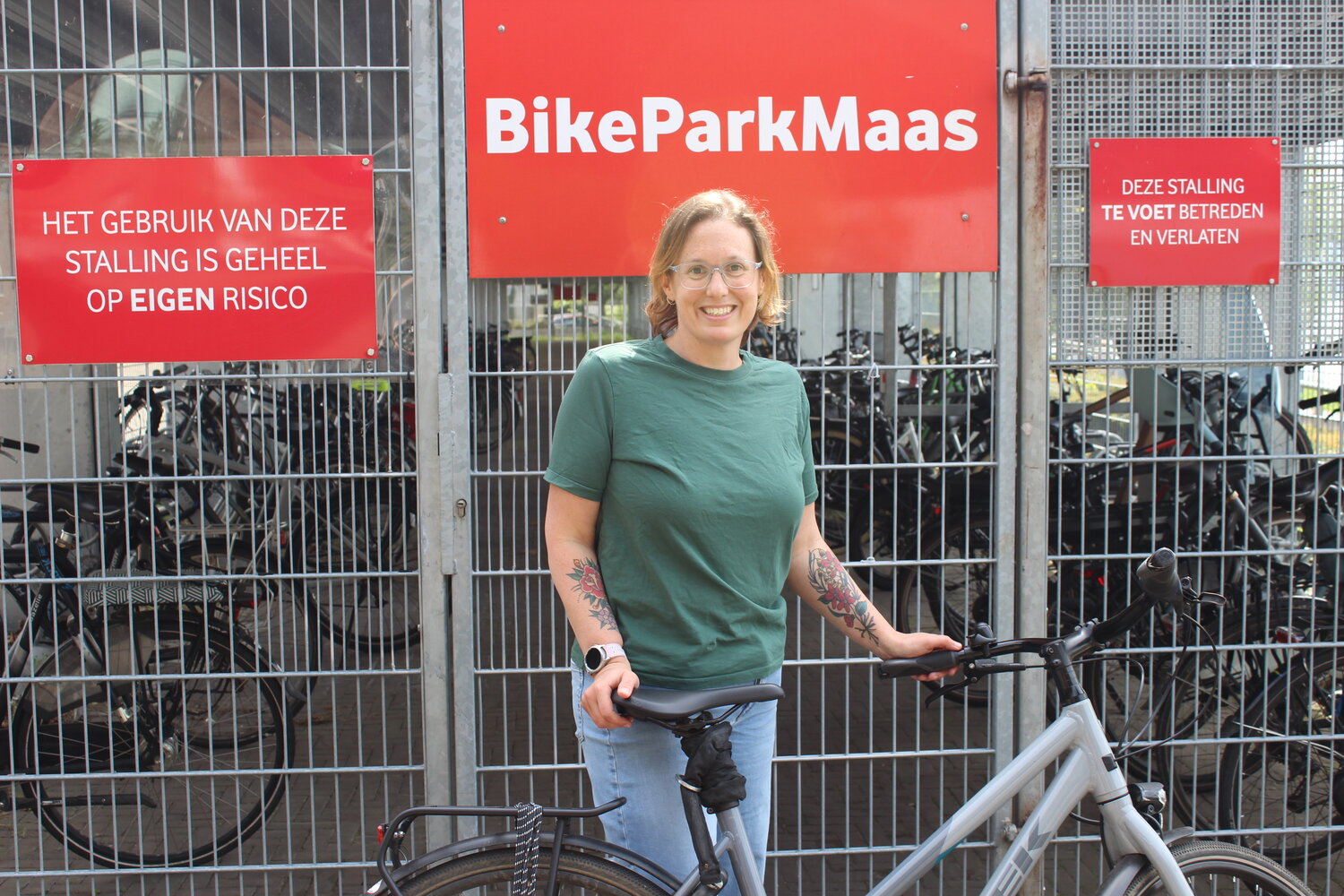 Joyce met haar fiets bij fietsenstalling Vodafone Maastricht. Achter haar een rood bord met BikeParkMaas 