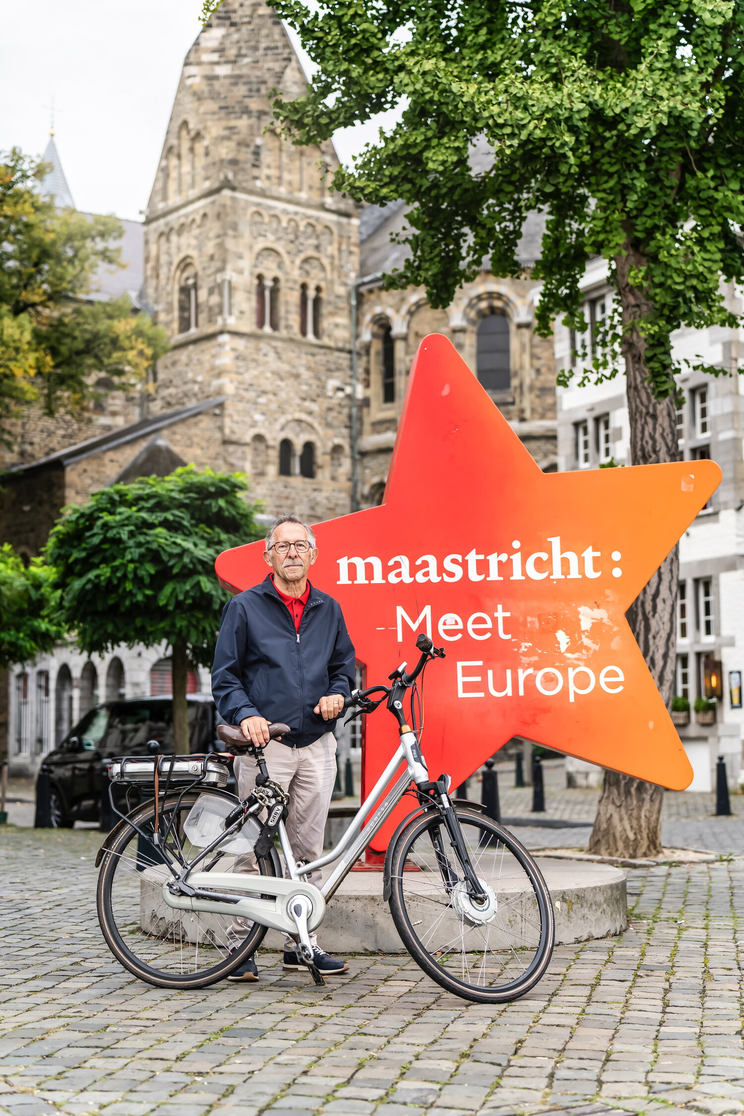 Jo Voorst met zijn fiets voor een kerk in Maastricht bij de ster met tekst Maastricht: meet Europe