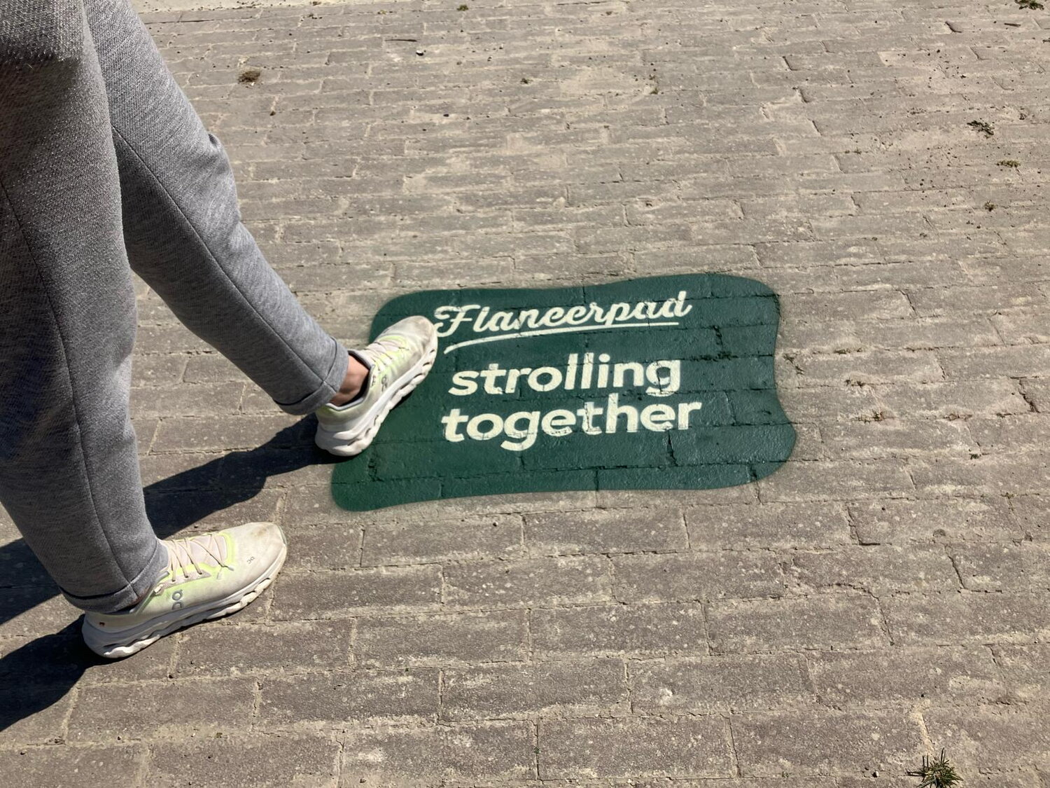 op een klinkerpaadje zie je de afdruk Flaneerpad stroming together en een voetganger die haar voet hierop zet