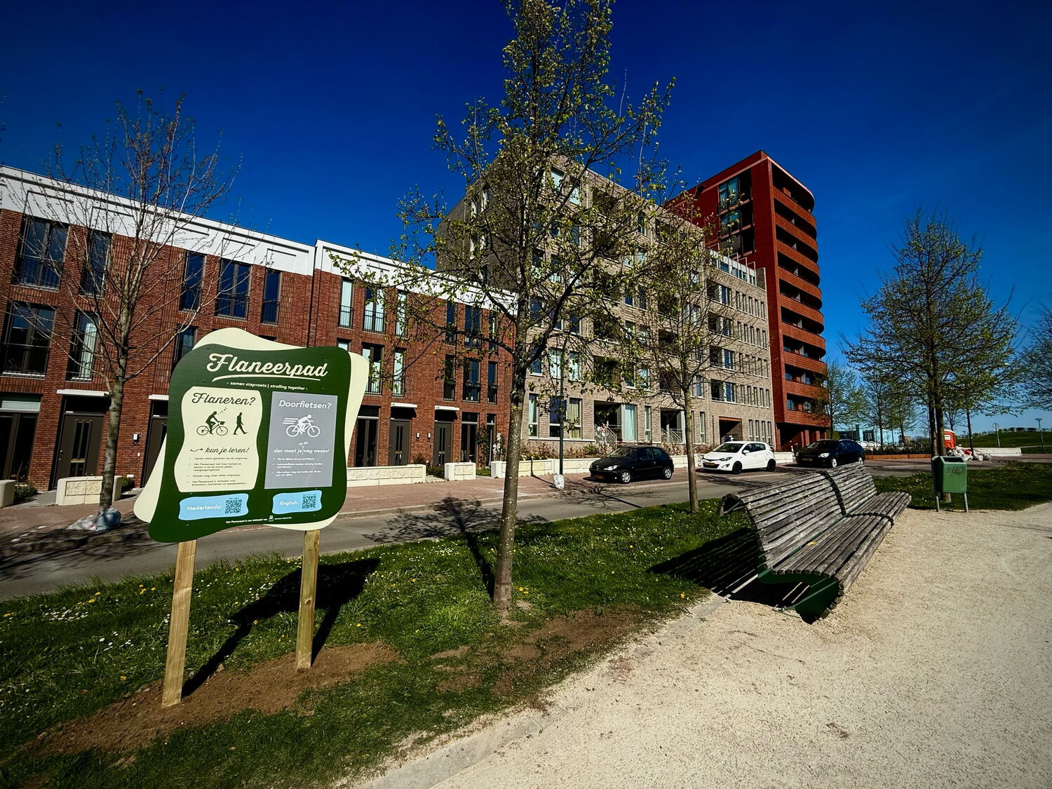 Aan de Groene Loper zie je een bord waarop staat hoe je het Flaneerpad gebruikt. Op de achtergrond nieuwbouwwoningen en een blauwe lucht