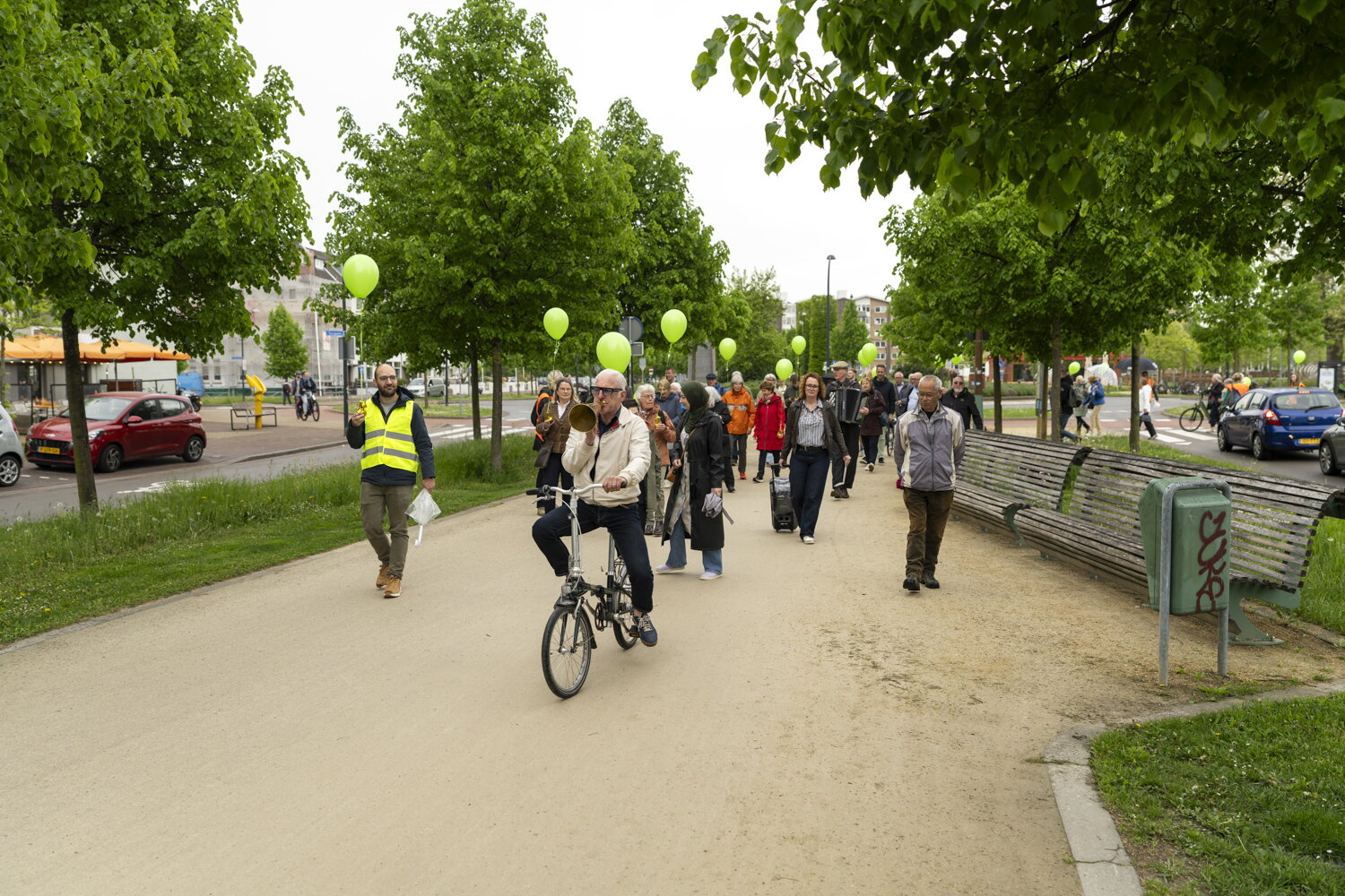 Een groep mensen met groene ballonnen loopt over de Groene Loper. Er fiets iemand voorop met een roeptoeter