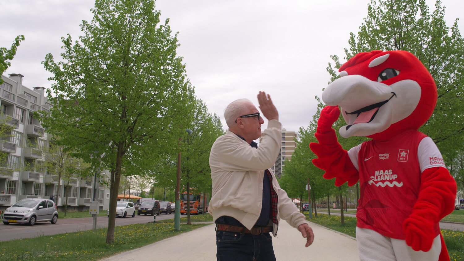 Een man in witte jas geeft een rode mascotte een high five op de Groene Loper