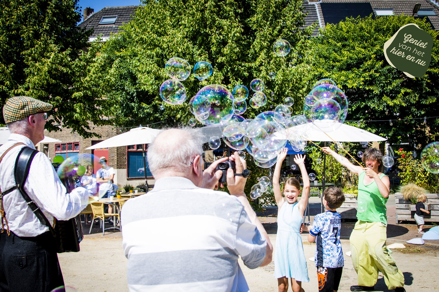 Kinderen spelen met grote zeepbellen terwijl een accordeonist erbij staat