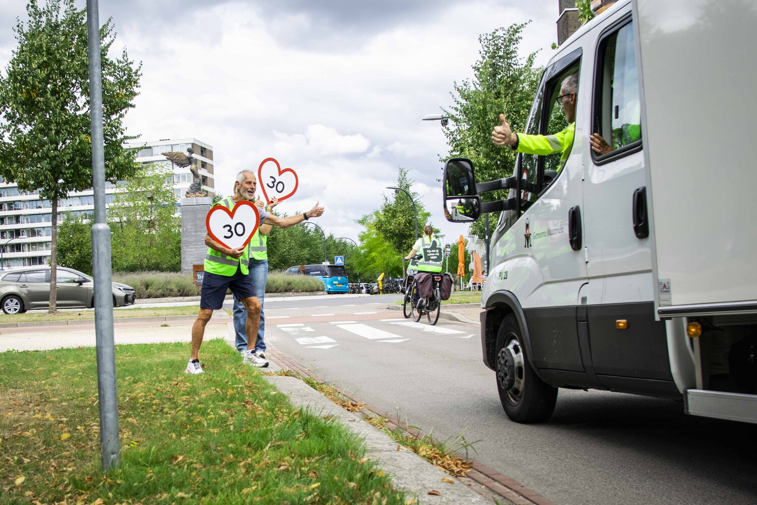 Flaneerpad Maastricht, man staat langs weg en steekt duim omhoog naar bestuurder busje die 30 rijdt zoals gewenst op rijbaan ernaast