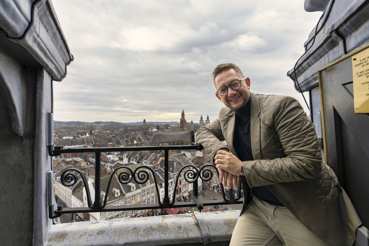 Frank Steijns in bruin jasje bovenop het gemeentehuis met Maastricht op de achtergrond