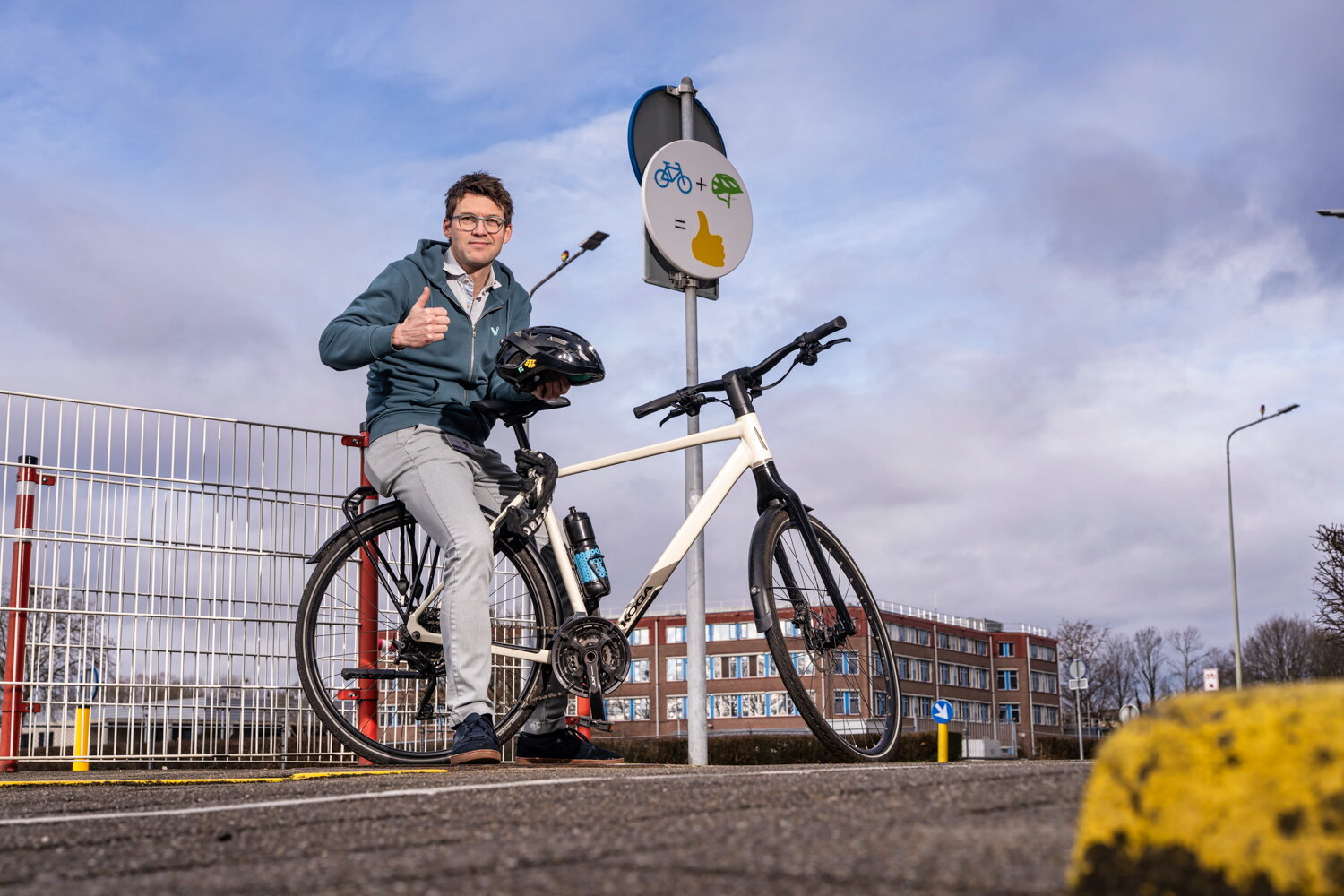 Marcel Aries met fietshelm in zijn hand en zittend op zijn bagagedrager. Hijs staat met zijn fiets langs de weg.